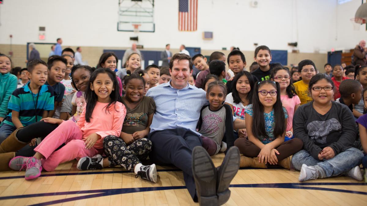Photo of Seth in a school gym surrounded by kids posing for a picture